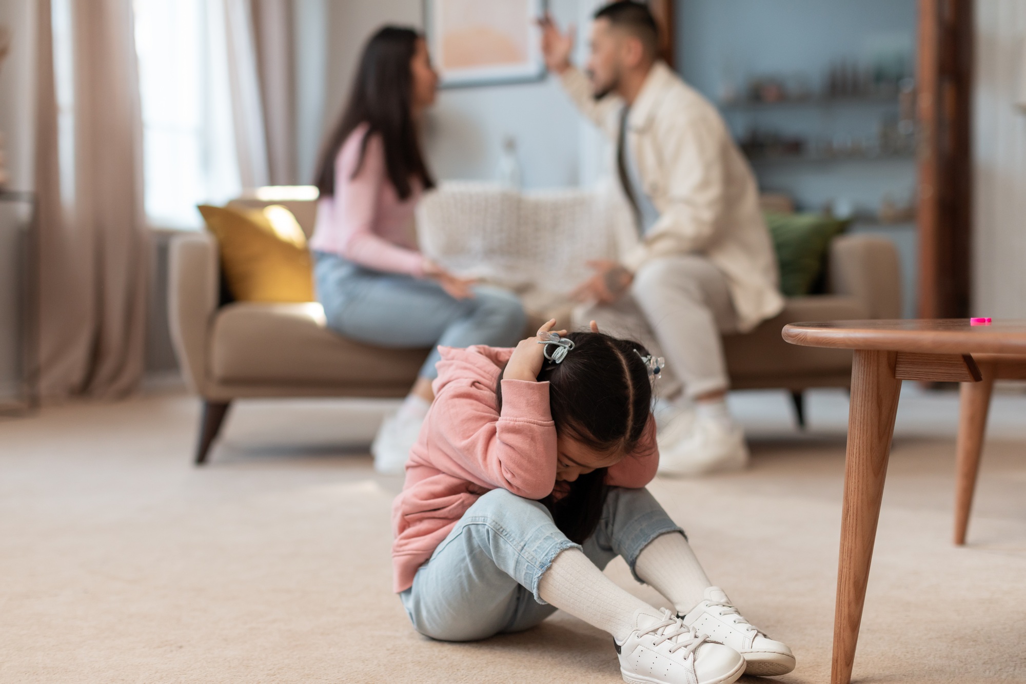 Asian baby covering ears while angry parents fighting at home